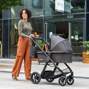 Babymore stylish black stroller with bassinet, designed for urban parents, offering comfort and convenience for newborns, photographed outdoors in front of a modern cafe.