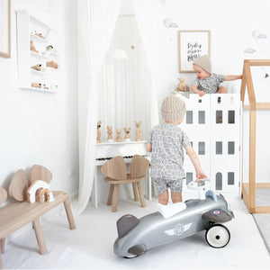 Toddler standing beside a silver Baghera ride-on plane in a stylish white nursery – vintage-inspired aircraft toy promoting balance and imaginative play for children aged 1 to 3 years