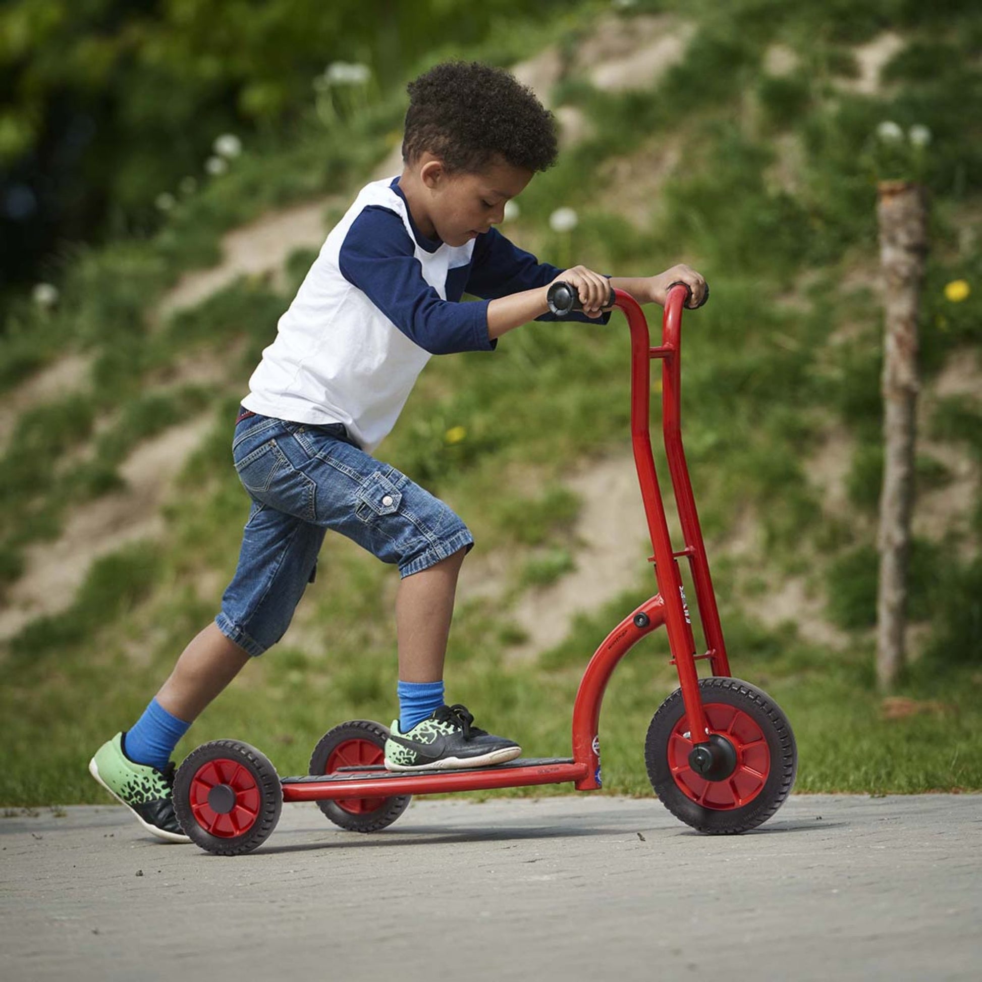 A boy riding a red Winther scooter, developing balance and coordination while enjoying outdoor play – available at Little Gliders.