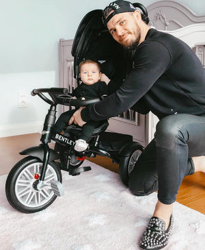 Murat Kazgan and his baby pose with the Bentley 6-in-1 Trike in Onyx Black, inside a nursery setting, showcasing the trike's comfort and craftsmanship.