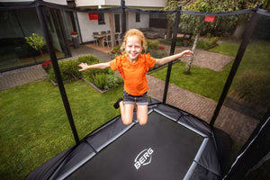 Happy child bouncing on a BERG trampoline with safety enclosure in a private garden, ideal for active play and outdoor fun.