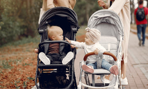 Two babies interacting in strollers during outdoor walk, toddler reaching out while parents stroll through park, emphasising baby connection and stroller comfort.