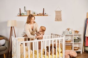 Mother placing baby in crib with soft toys – Little Gliders nursery essentials for cosy and safe sleep.
