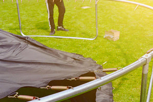 Trampoline assembly in progress showing frame and coiled springs on grassy lawn, illustrating setup of outdoor garden trampoline.
