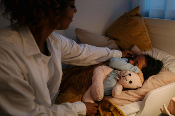 Parent gently tucking in a sleeping child cuddling a plush teddy bear, highlighting Little Gliders’ cosy and comforting sleep essentials for peaceful bedtimes