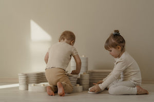 Two young children playing with natural wooden stacking toys on the floor, developing fine motor skills, creativity, and concentration in a calm nursery setting.