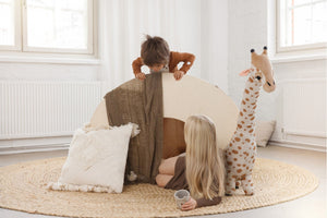 Two young children playing with a minimalist wooden climbing toy in a calm, Scandinavian-inspired playroom with neutral tones, soft textiles, and a plush giraffe.