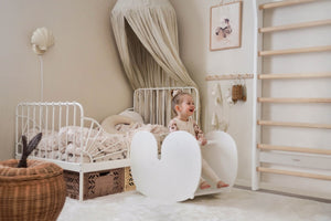 Child playing in a Montessori-style bedroom with toddler bed, wooden rocker, and wall bars—showcasing grow-with-me furniture for a big kid room transition.