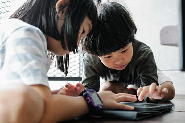 Two young children intently using a tablet on the floor indoors – a visual example for parents exploring how to limit screen time for kids and encourage more physical play and screen-free activities.