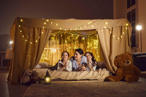 Mother and daughters inside a cozy blanket fort with fairy lights – magical bedtime bonding moment