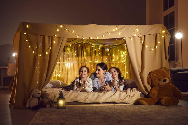 Mother and daughters inside a cozy blanket fort with fairy lights – magical bedtime bonding moment
