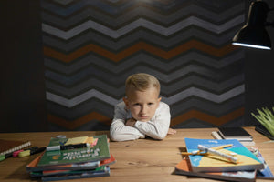 Bored-looking child sitting at a desk with school books and no devices, symbolising the power of unstructured time and imaginative thinking