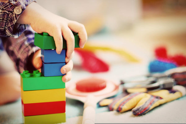 Close-up of a child's hand stacking colourful building blocks in a play corner, showing calm, focus and independent play in a home setting