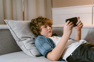 Young boy lying on sofa using a smartphone, highlighting modern screen time habits and the need for mindful play alternatives
