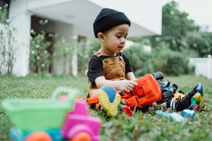 Toddler playing with colourful plastic toy vehicles on grass, representing outdoor play, imagination and active childhood exploration