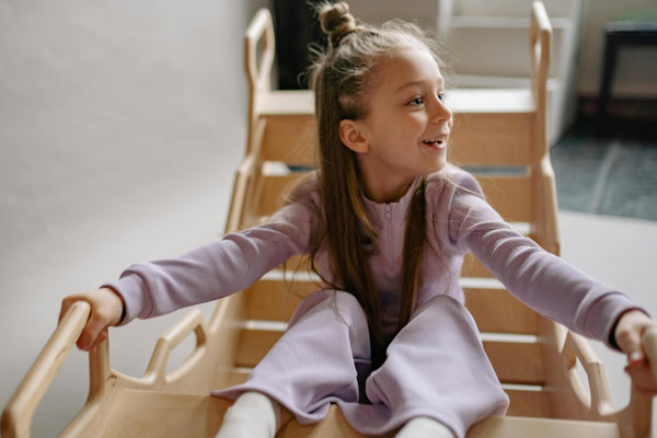 Smiling girl playing on indoor wooden climbing toy, holding handles for balance, encouraging active and imaginative play at home.