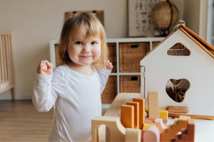 Smiling toddler playing indoors with a wooden toy house, representing calm, confident play and purposeful indoor learning