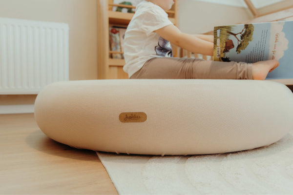 Child reading on Jupiduu soft pouf in calm Montessori playroom – round floor cushion for toddlers to relax, read and unwind in sensory-safe space