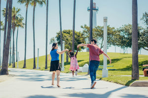 Joyful family walking outdoors with a child swinging between parents, symbolising playful movement and the stages of childhood growth