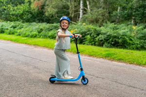 Smiling girl riding blue kids' electric scooter outdoors – safe and fun e-scooter for children with helmet protection and lightweight design
