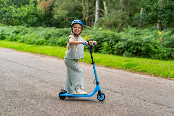 Smiling girl riding blue kids' electric scooter outdoors – safe and fun e-scooter for children with helmet protection and lightweight design