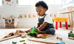 Young child sitting on a carpeted floor, focused on playing with a wooden train set, promoting open-ended play and early learning with toys from Little Gliders.