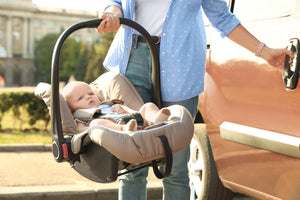 Parent placing a baby in an infant car seat next to a parked car, highlighting the importance of secure newborn travel systems