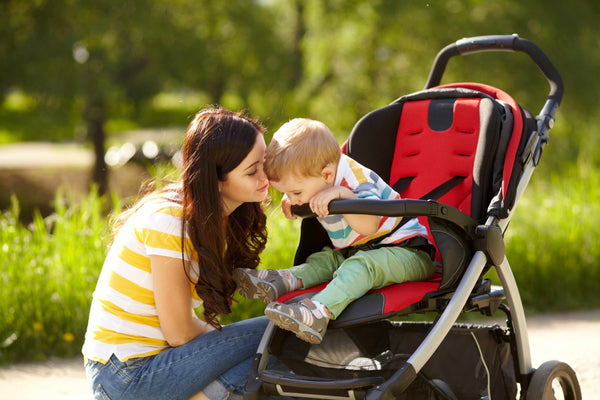Mother comforting toddler in red and black stroller – outdoor bonding moment on a sunny day