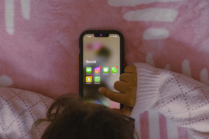 Child using smartphone with social media apps open on a bed, illustrating concerns around screen time, mood and sleep in children
