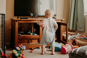 Toddler standing near a television surrounded by toys, representing the contrast between screen time and active play in early childhood