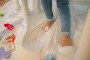 Close-up of child's legs with colourful sensory blocks in sand, representing tactile exploration and sensory play across different ages