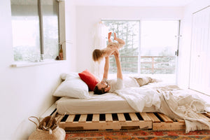A father lifting his toddler in a bright, cosy bedroom — representing joyful bonding and the transition from cot to toddler bed in a nurturing environment.