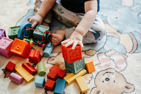 Toddler playing with colourful building blocks on a nursery rug, illustrating non-toxic toy cleaning and eco-friendly toy care tips for parents