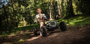 Child riding a BERG Buddy Jeep Wrangler go-kart on a forest trail, showcasing its rugged design and off-road capabilities.