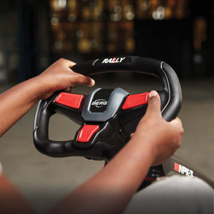 Hands gripping a BERG Rally steering wheel with ergonomic design and vibrant red accents.