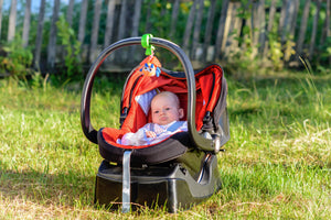 Baby sitting comfortably in a red car seat with a toy attached, ideal for safe and secure travel – available at Little Gliders.