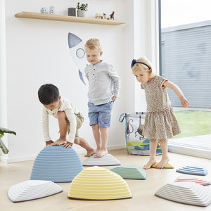 Three young children balancing on pastel-coloured Gonge Riverstones during indoor play, promoting coordination, movement, and sensory development through toy bundles from Little Gliders.