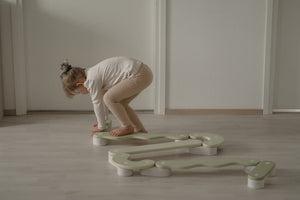 A child focused on assembling modular wooden balance beams in a simple, child-friendly room, promoting motor skill development and active play.