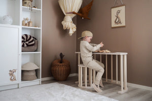 A child playing at a wooden table in a Scandinavian-style bedroom, surrounded by natural decor and toys, promoting creativity and a simple, nurturing environment. fitwood luoto stool little gliders