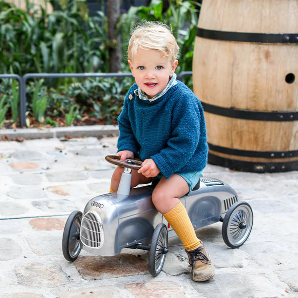 Young child riding a silver Audi Baghera ride-on car outdoors – officially licensed vintage-style metal toy vehicle for toddlers, designed for imaginative play and developing motor skills