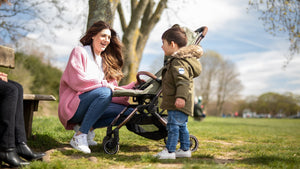 Mother laughing with her young child next to a Didofy award-winning pushchair in a park, showcasing British-made quality and family-friendly design.