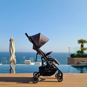Didofy Aster 2 lightweight stroller by the pool, showcasing its sleek, portable design with a scenic ocean backdrop.