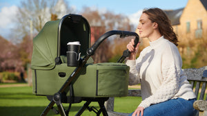 Mother sitting on a park bench, relaxing with a Didofy stroller beside her, showcasing the ergonomic handle and integrated cup holder.