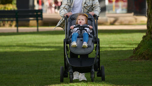 Toddler comfortably seated in a stroller being pushed through a grassy park, showcasing stroller’s smooth ride and child’s happiness.