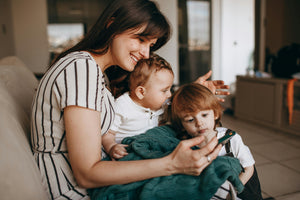 A mother smiling while sitting with her two children, bonding over a shared activity on a smartphone.