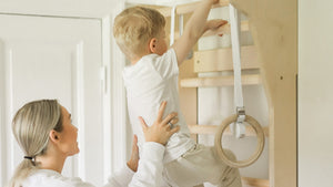 Mother helping her young child climb FitWood wall bars in a home setting, promoting active play and fitness for kids.