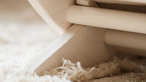 Close-up of the wooden leg and frame of a FitWood rocking chair on a soft, textured rug.