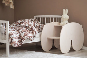 A charming wooden rocking chair or horse in table form beside a toddler’s bed adorned with teddy bear patterned bedding, creating a cosy and playful atmosphere in a child’s room.