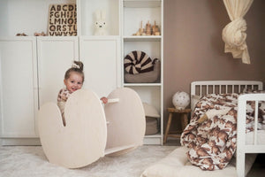 A smiling toddler plays on a wooden rocking chair or horse in a beautifully decorated nursery, featuring soft textures, a neutral colour palette, and playful decor.