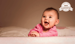 Smiling baby in a pink onesie with a 100% money-back guarantee badge in the corner, symbolising a happy child guarantee offered by Little Gliders
